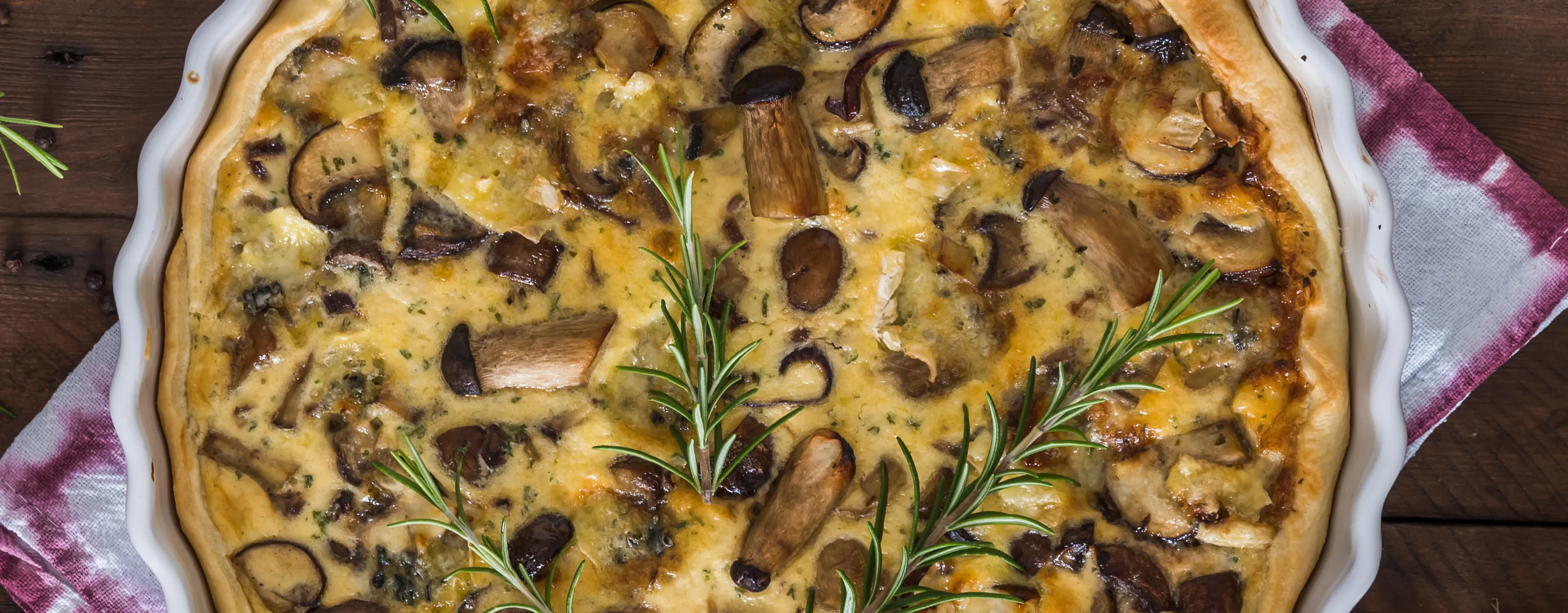 Baked mushroom quiche with a golden crust, garnished with herbs.