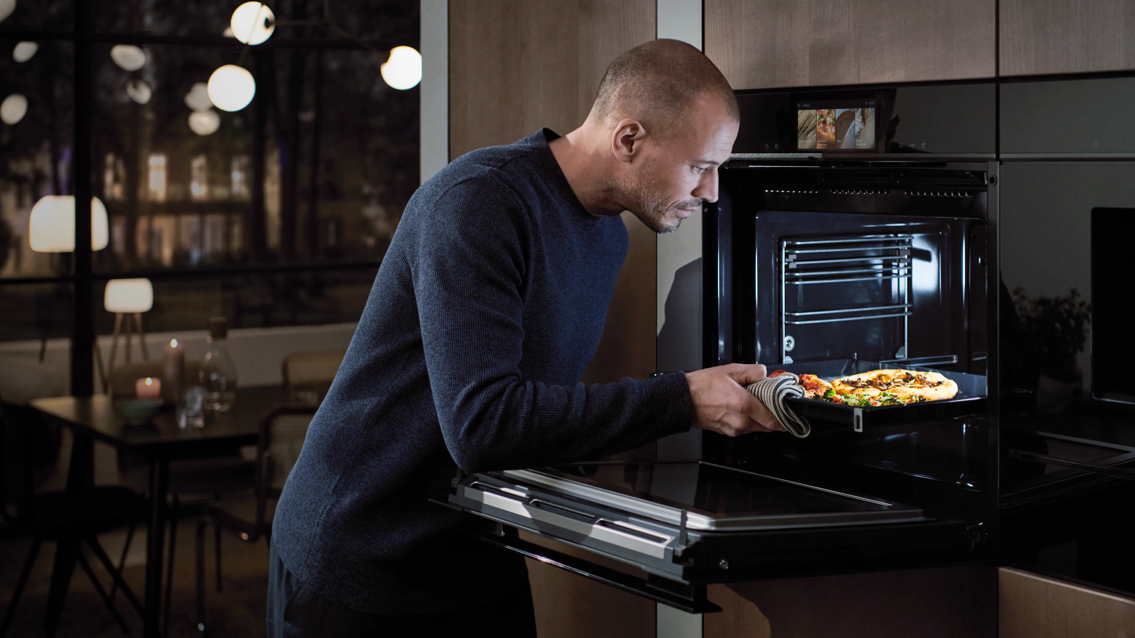 A man removing a cooked focaccia bread from a Siemens iQ700 oven.
