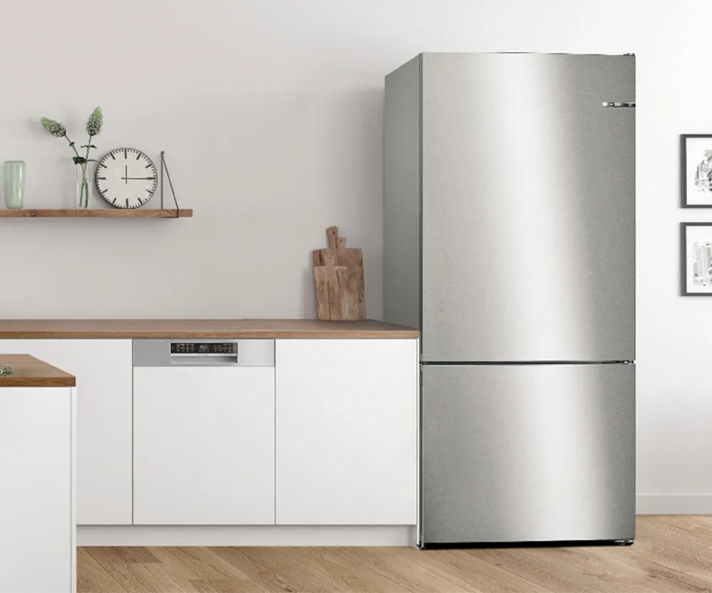 A modern kitchen with a stainless steel Bosch fridge-freezer, an integrated Bosch dishwasher, white cabinets, and light wooden countertops, decorated with a clock and plants.