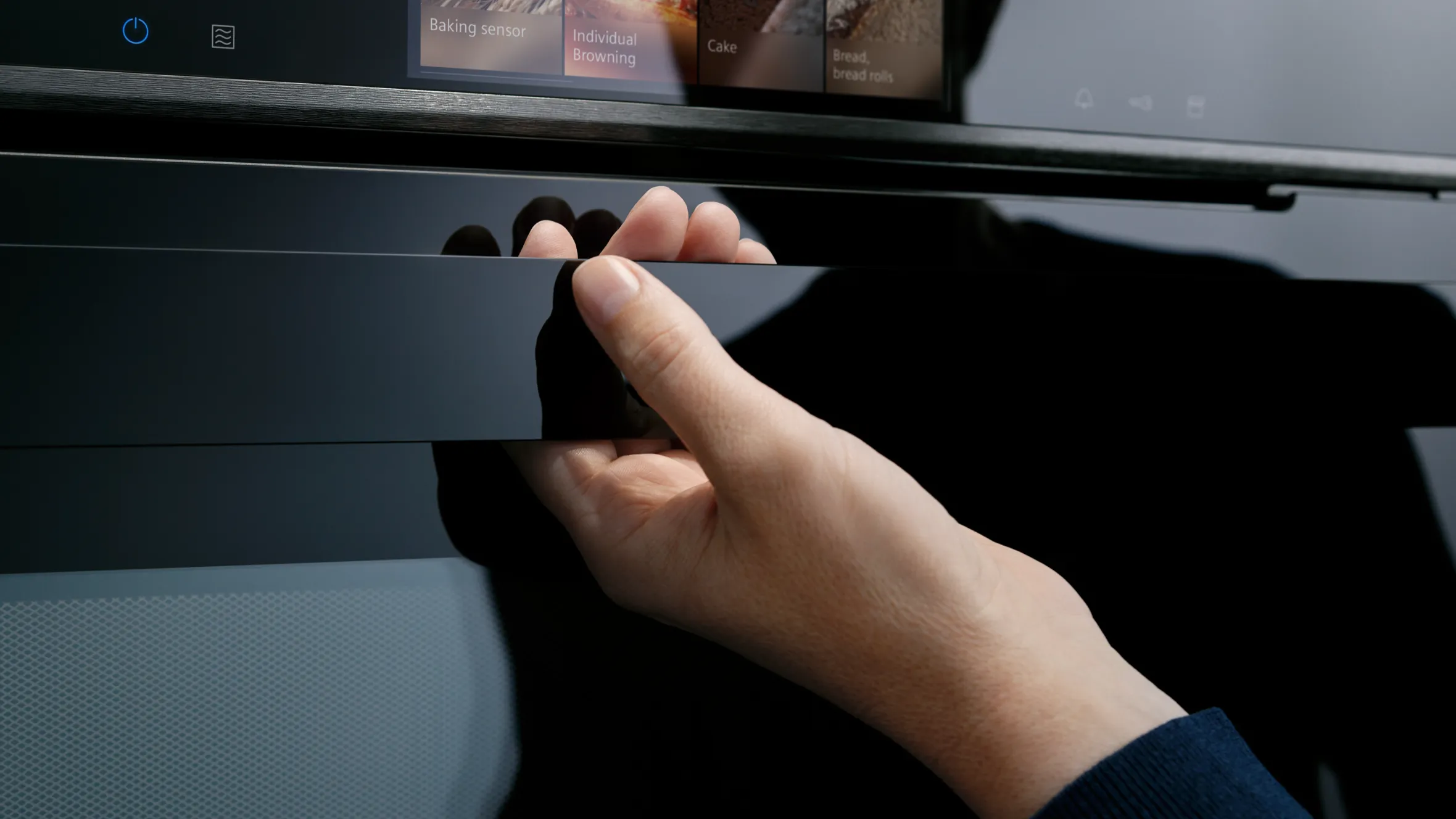 Hand reaching to open a drawer on a dark-colored cabinet or storage unit.