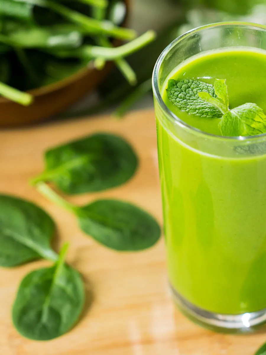 A green avocado smoothie standing on a table with spinach leafs next to it.