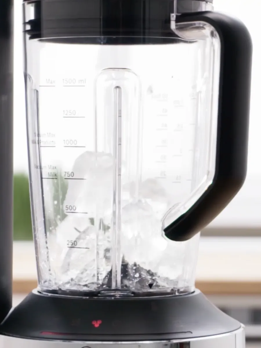 Container mixer de sticlă cu cuburi de gheață și lichid interior, bază blender vizibil.