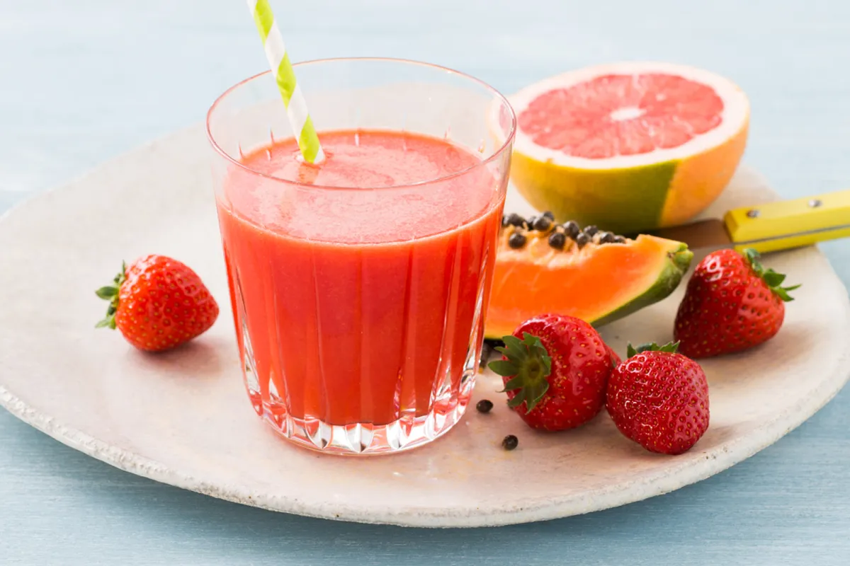 A yummy red juice standing on a plate with fresh fruits.