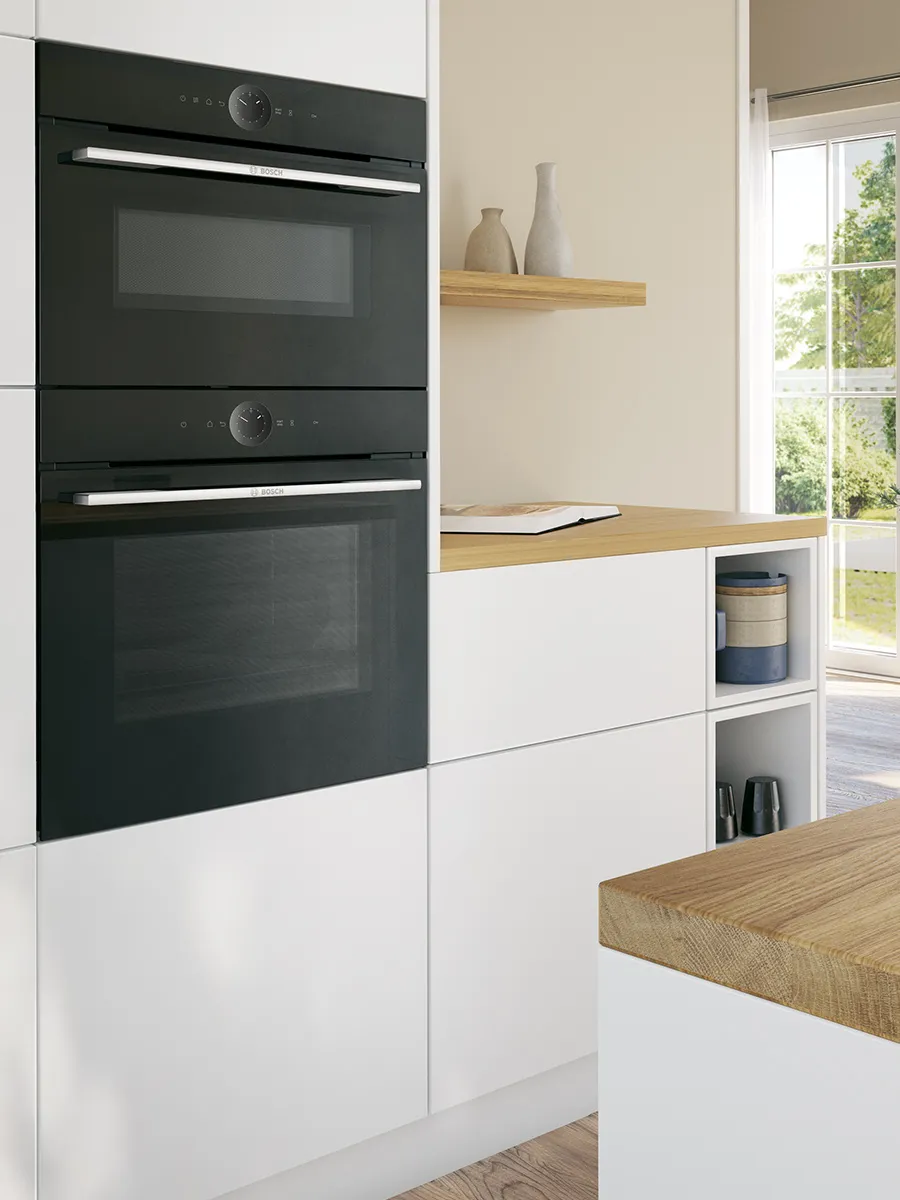 Modern kitchen with two black built-in ovens, wood countertop, white cabinets, and natural light.