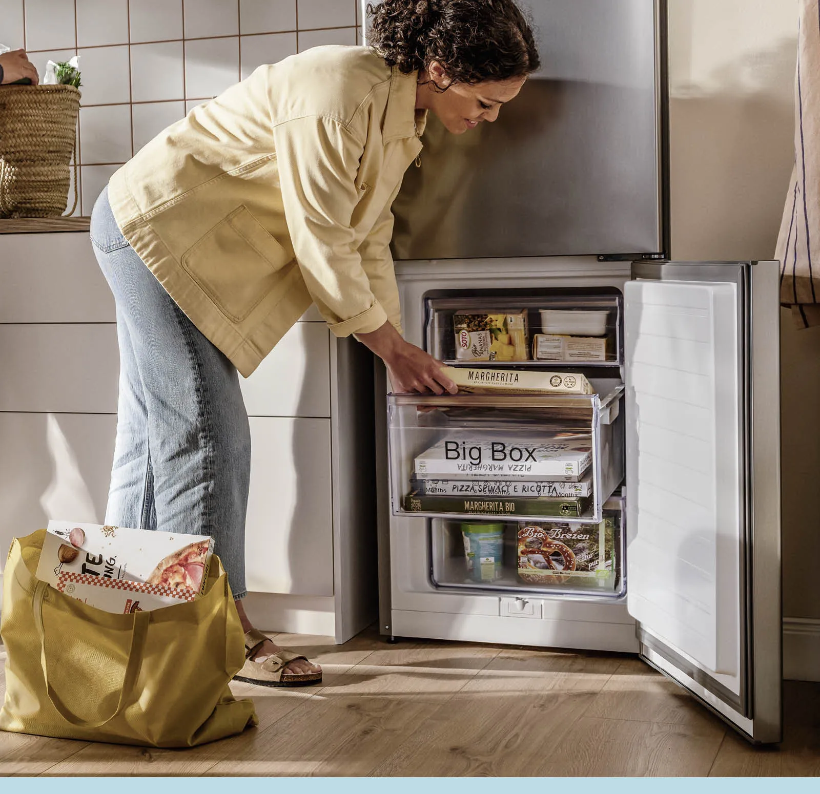 Frau sortiert Tiefkühlpizzen in die Schubladen eines geöffneten Gefrierschranks ein
