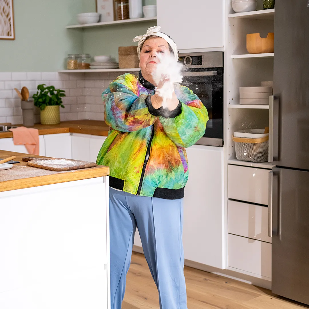 Gramdin colorful jacket claps hands, releasing flour in a modern kitchen.