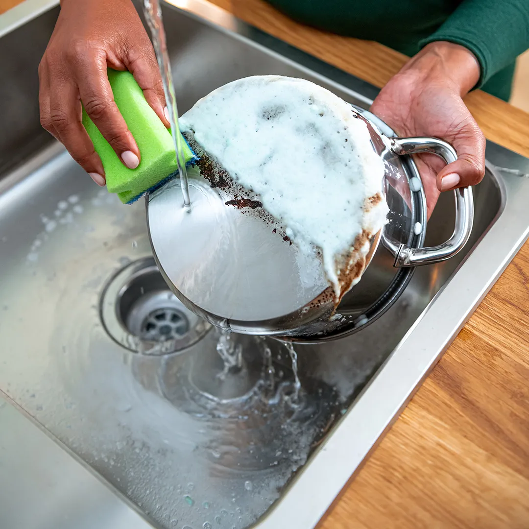 Grandma cleaning grease off pot with sponge, soap and water