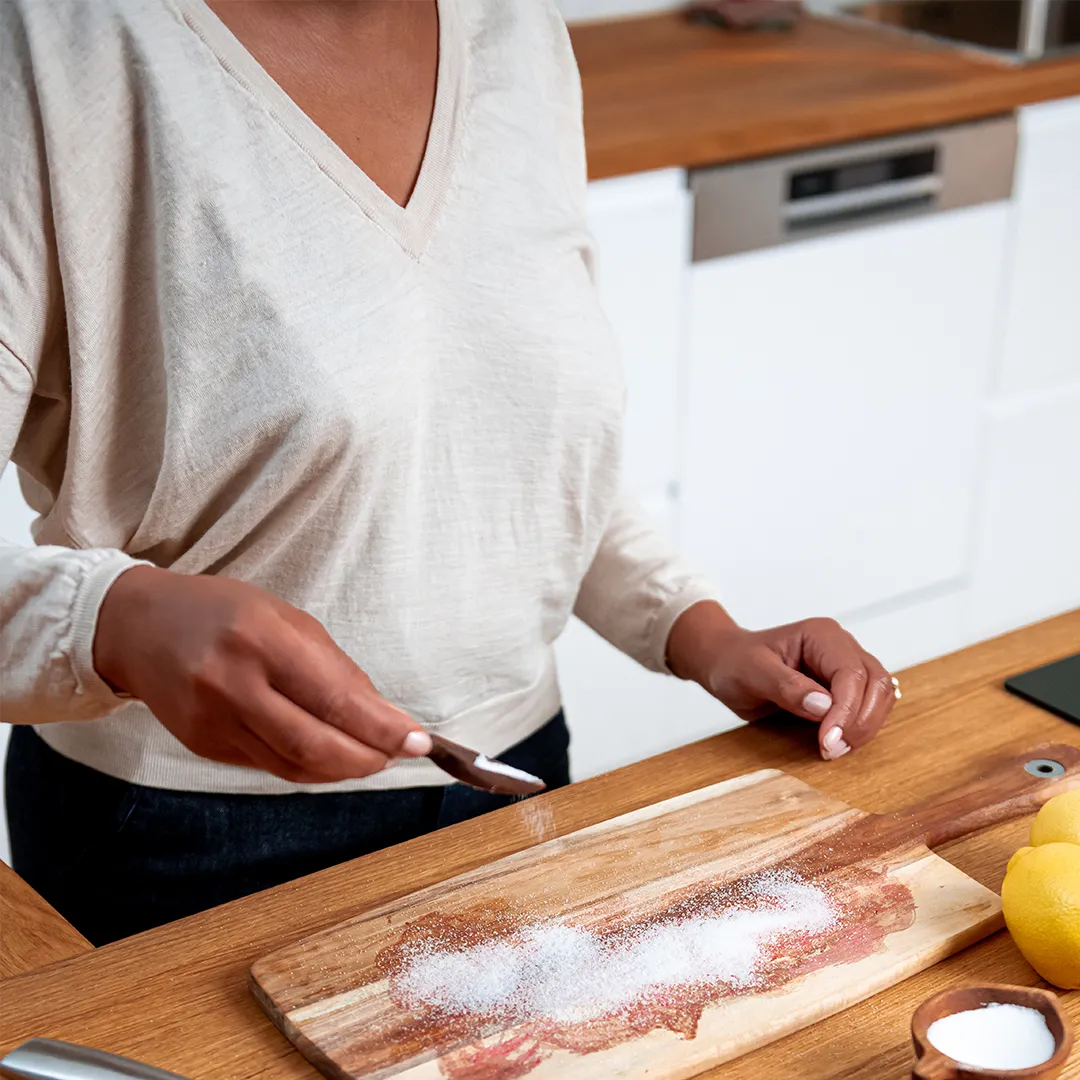Person seasoning a wooden cutting board with spices in a modern kitchen.