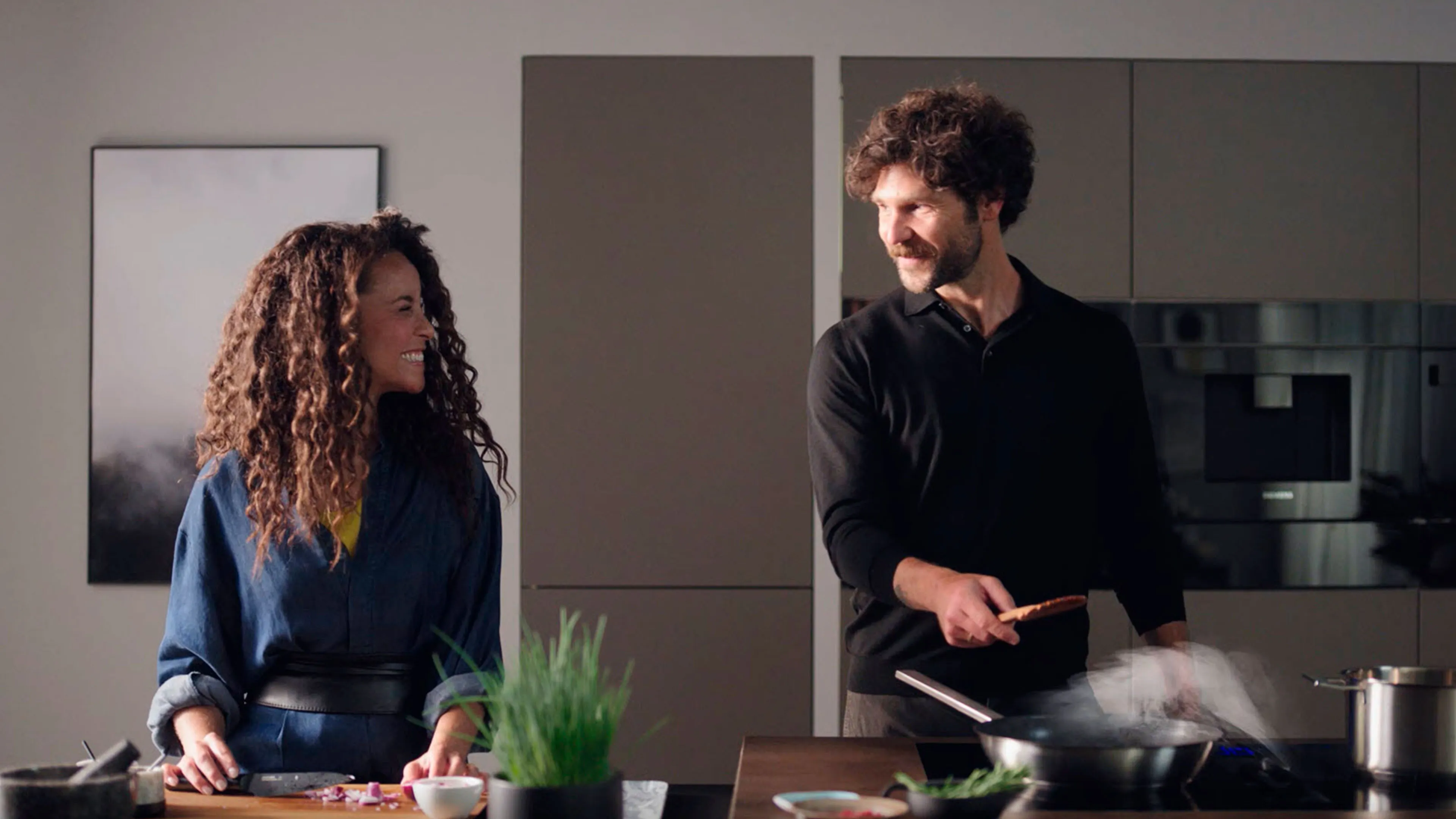 Et par står i et moderne køkken og laver mad med et smil. Køkkenet er udstyret med Siemens-produkter.