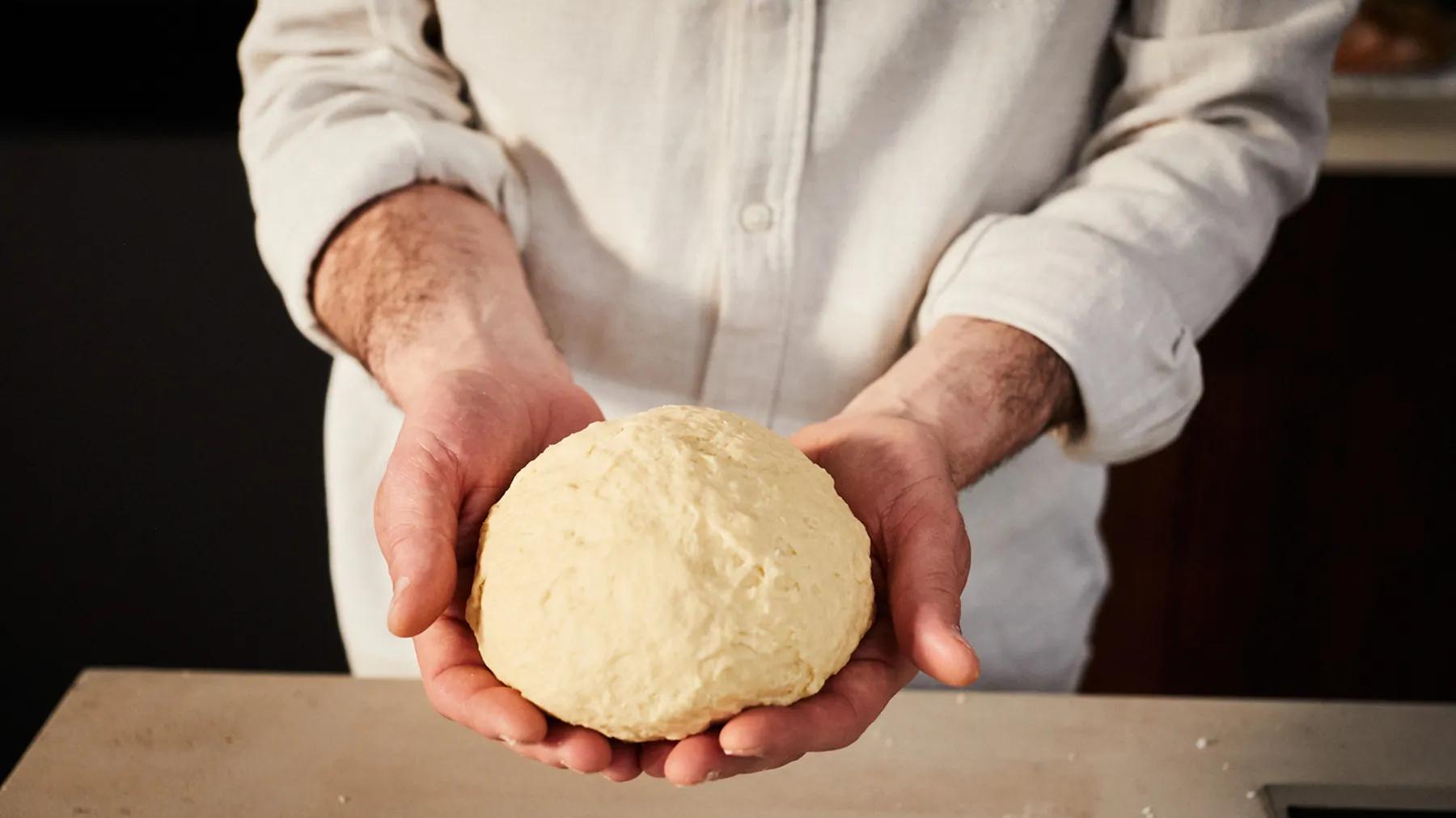 Chef's hands holding freshly kneaded dough on wooden surface.