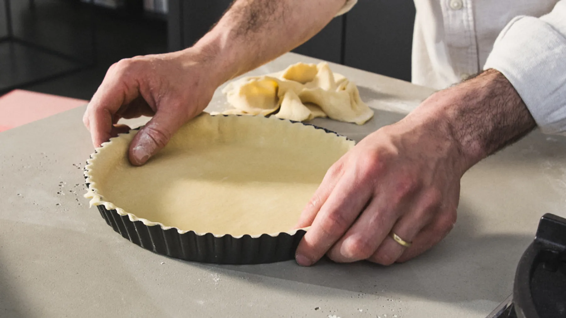 Hands preparing a pastry crust in a kitchen setting.