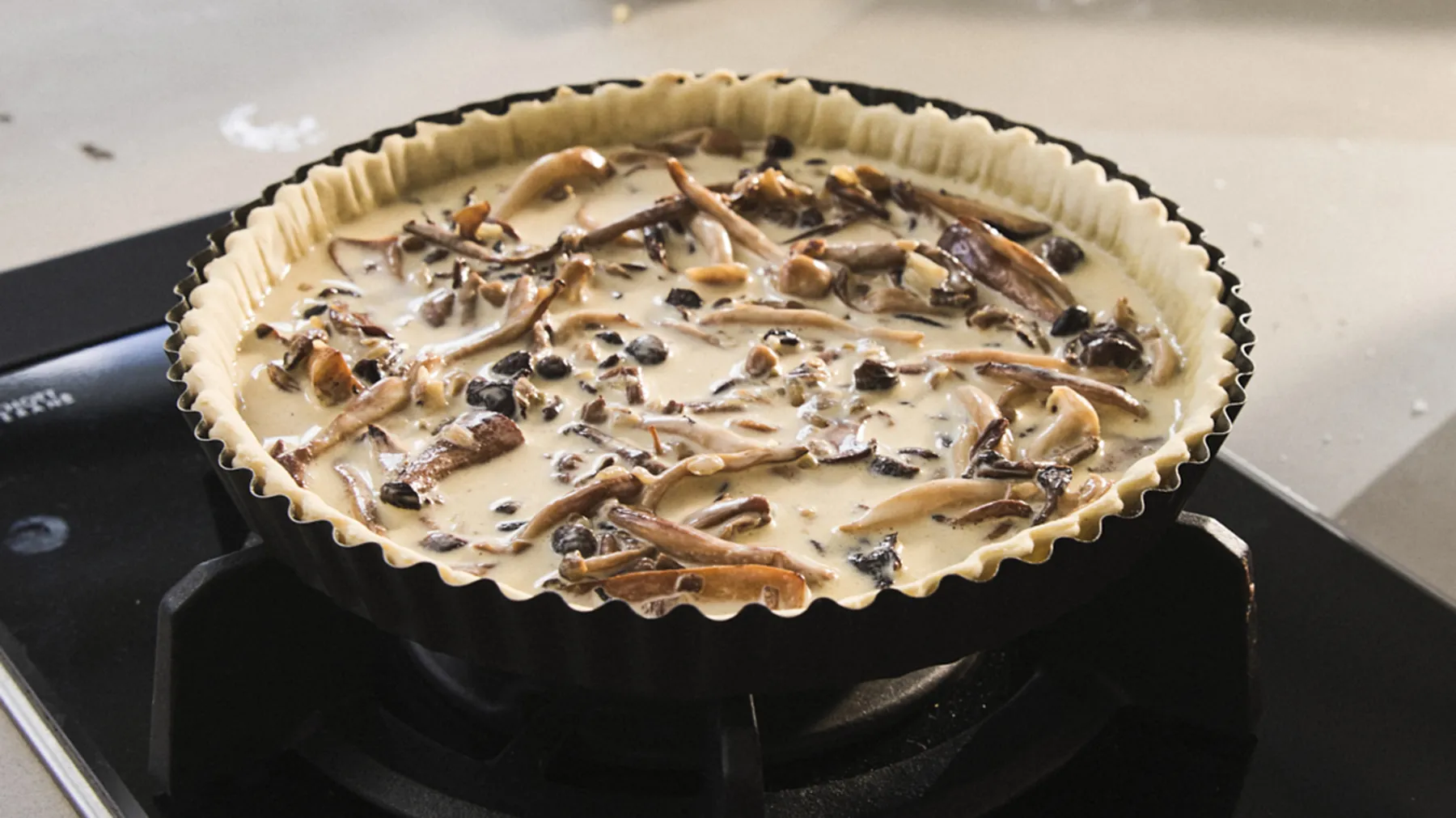 Baked pie with mushrooms and other ingredients in a black pie dish on a stove.