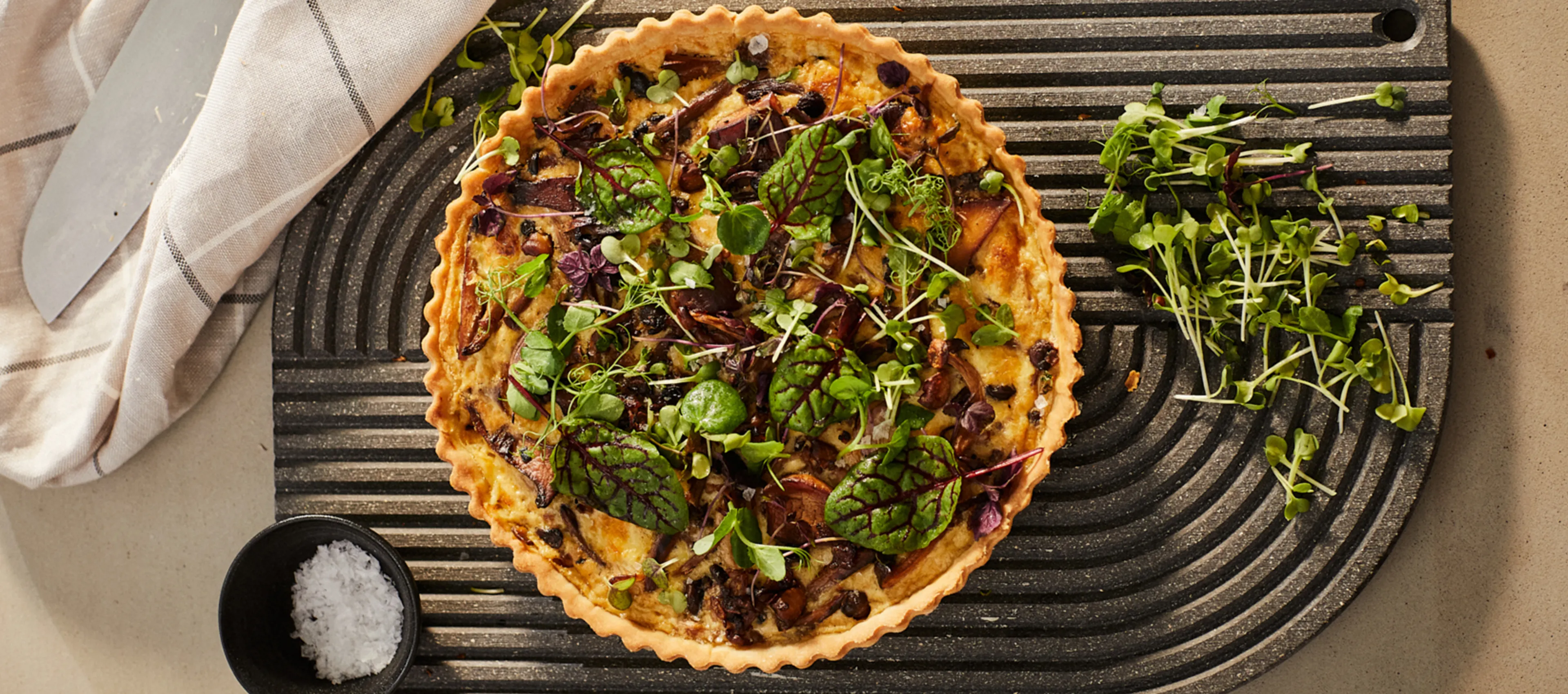 Savory quiche with greens, herbs, and a flaky crust on a dark baking tray.