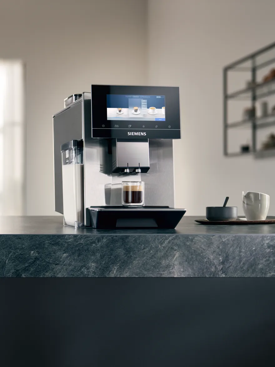 Kávovar Siemens eq stojí na kuchyňské lince, pod výpustí je připravená káva.