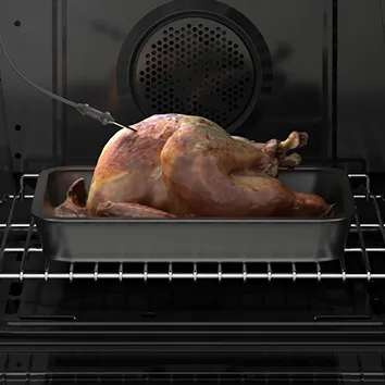 Chicken roasting in an oven with a meat thermometer inserted, placed on a Bosch oven rack.