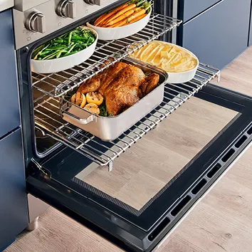 Open oven with roasted chicken, vegetables, and gratin dishes on wire racks.