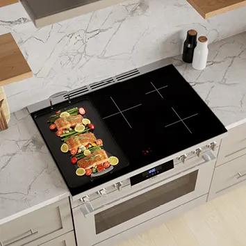 Modern kitchen with a black Bosch induction cooktop and a grill plate with vegetables and meat.