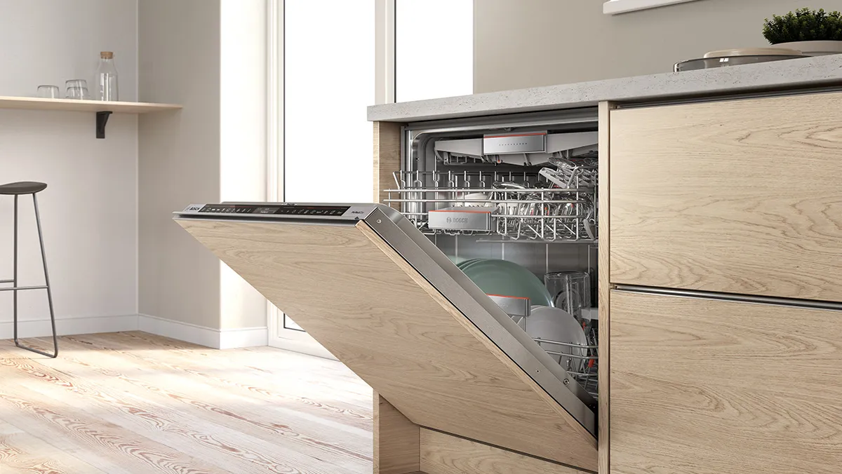 A partially open, built-in Bosch dishwasher in a modern kitchen with wooden cabinets and a visible rack of dishes.