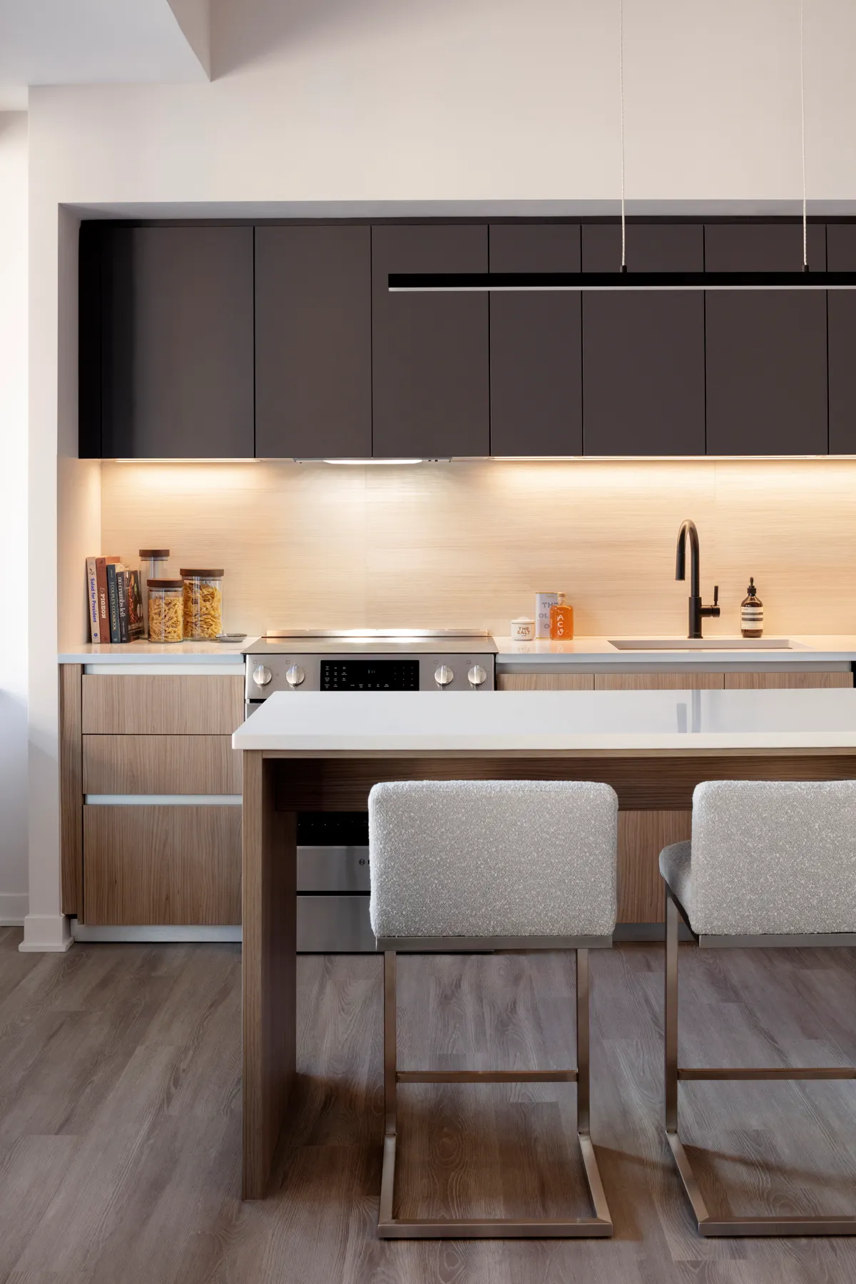 Modern kitchen with dark cabinets, stove, island, and two cushioned chairs.