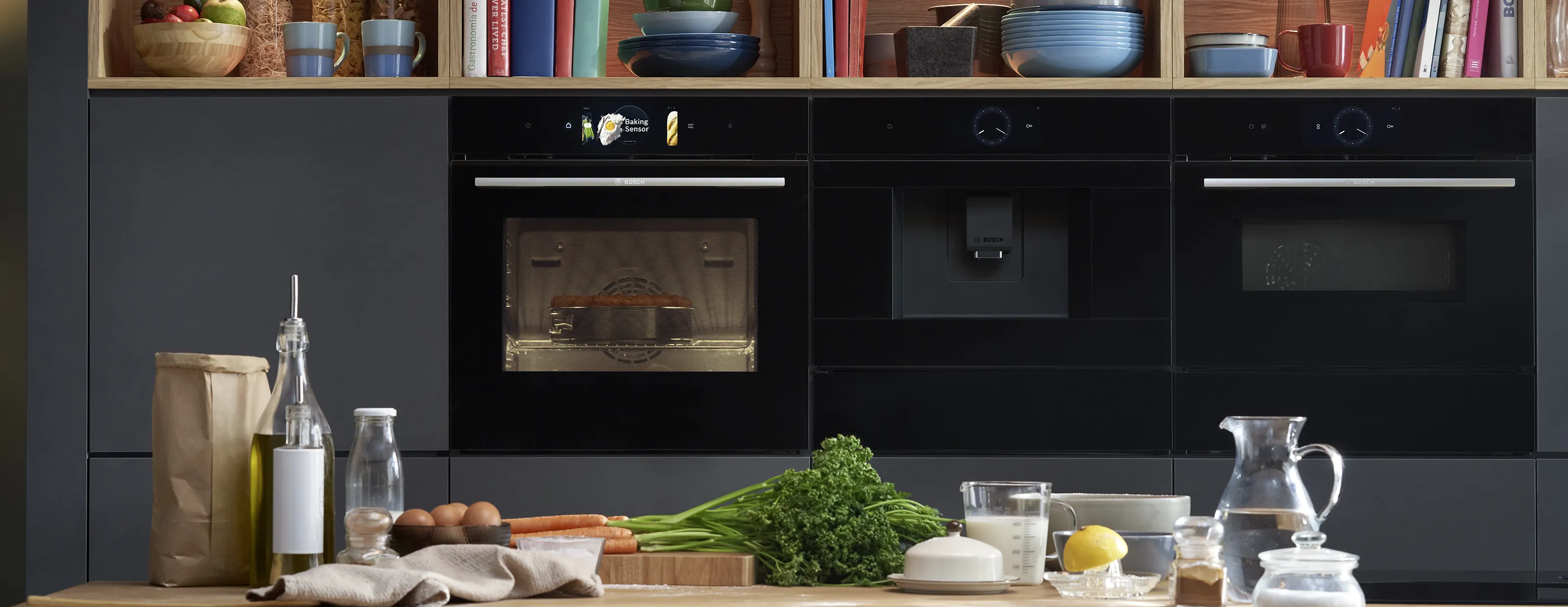 Modern kitchen with black cabinets, shelves, cooking appliances, and various food ingredients on the counter.