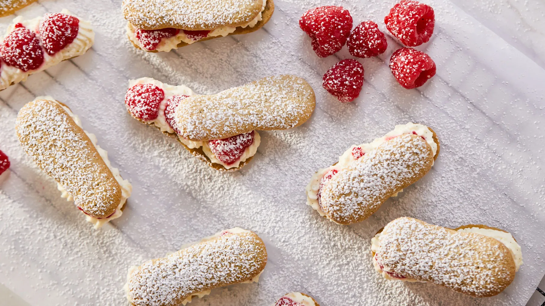 Powdered sugar-coated pastries with fresh raspberries on a marble surface.