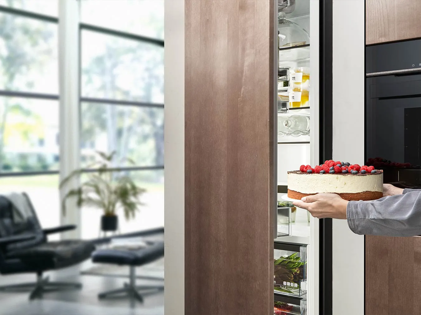 Persoon halen taart uit koelkast in moderne keuken met groot raam.
