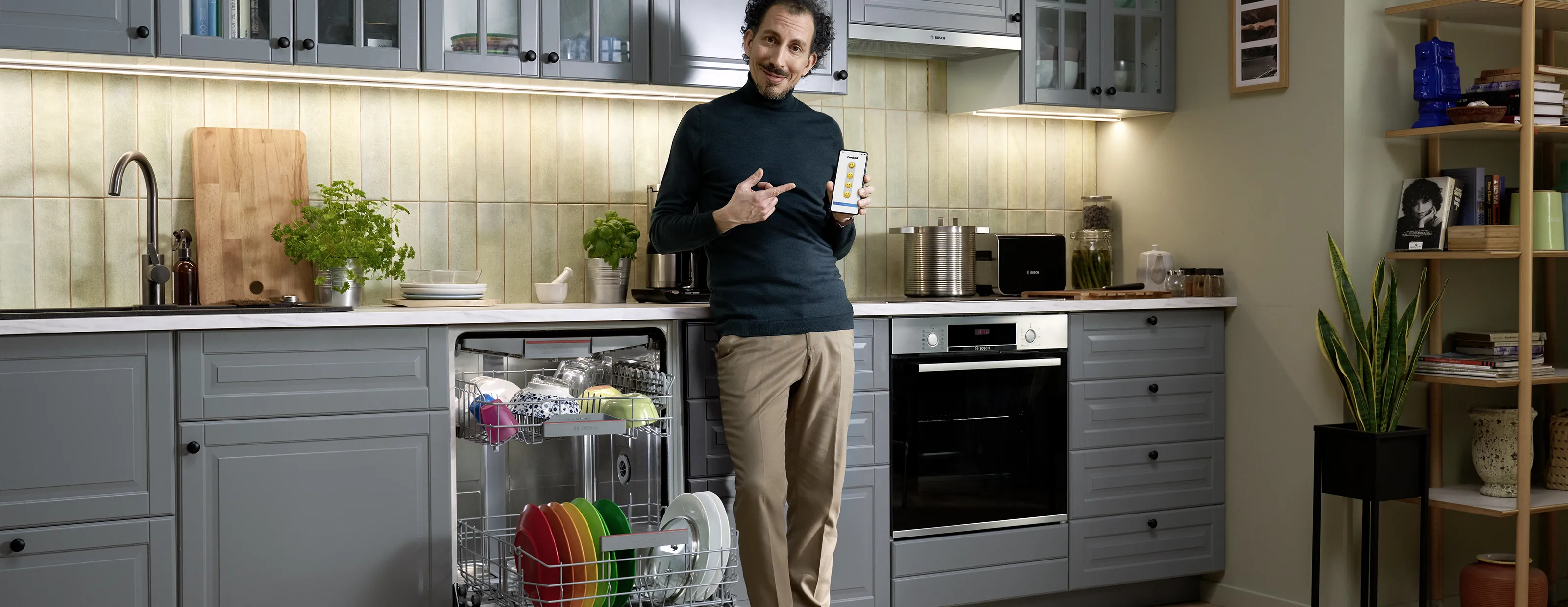 Man in kitchen using smartphone near open dishwasher with dishes.