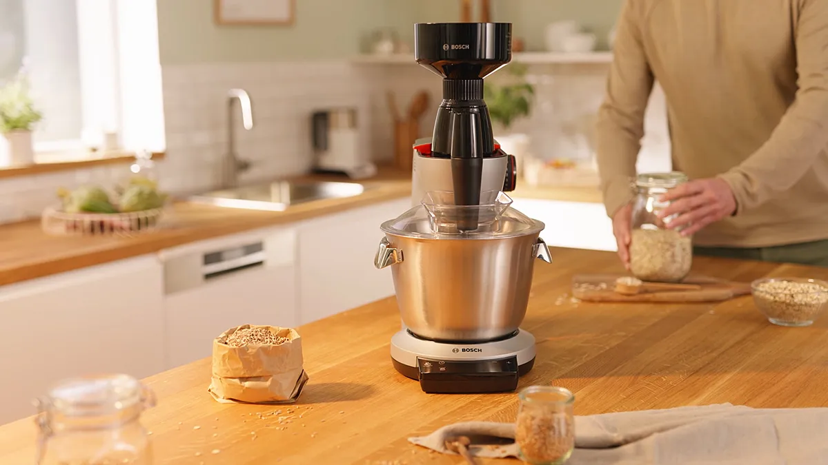 Kitchen counter with stand mixer, baked goods, and person's hands in frame.