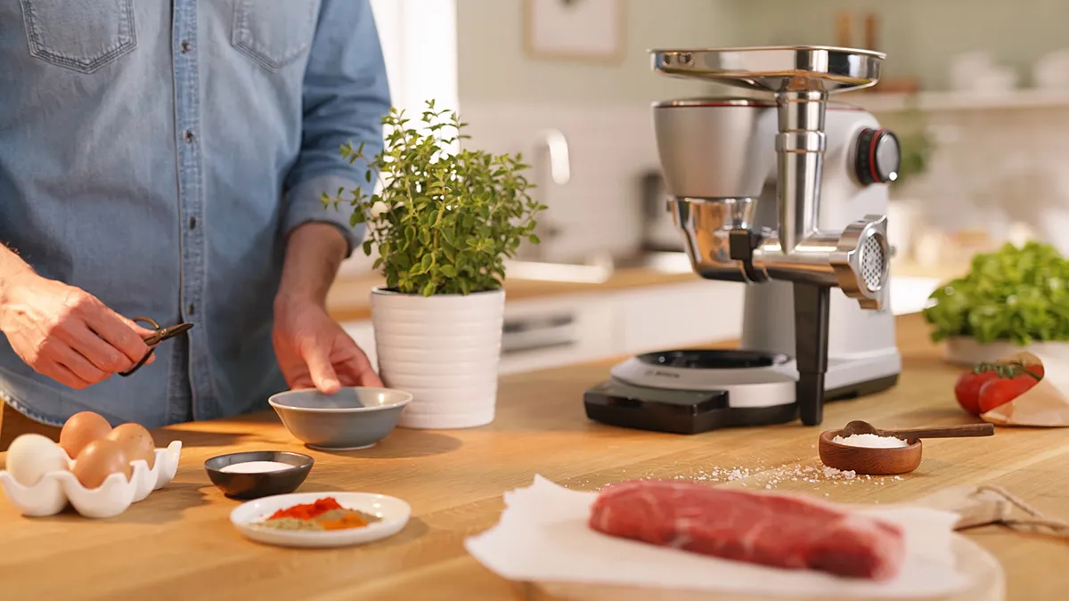 Kitchen counter with cooking appliances, fresh ingredients, and a person's hands preparing food.
