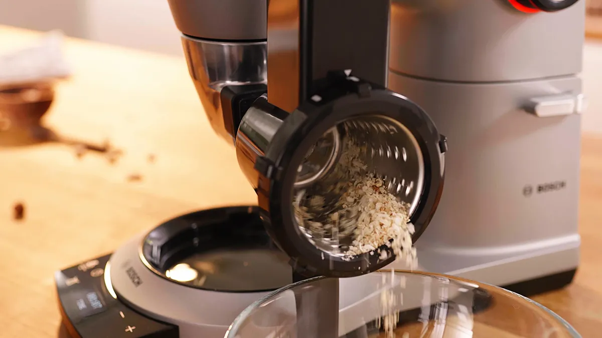 Coffee grinder pouring ground coffee into a glass container on a kitchen counter.