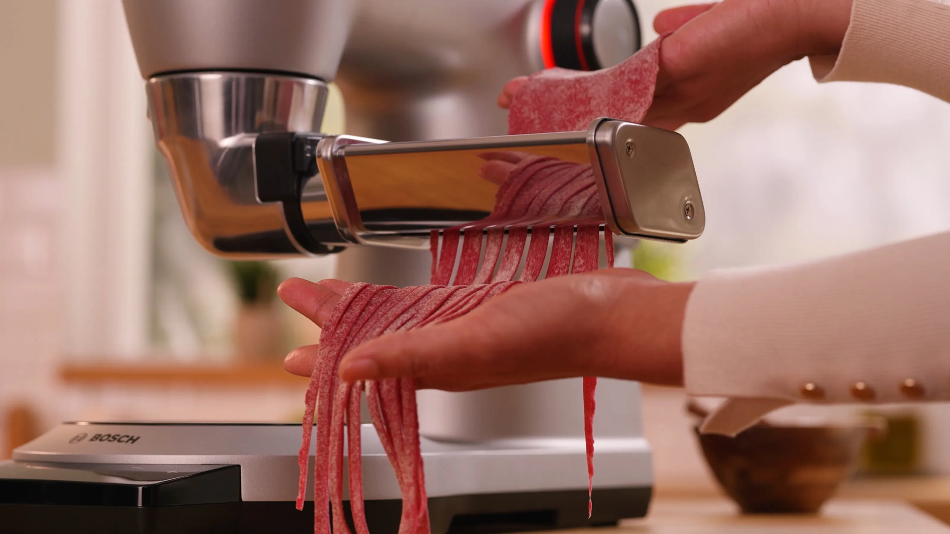 Pasta maker extruding fresh red dough from a kitchen appliance.