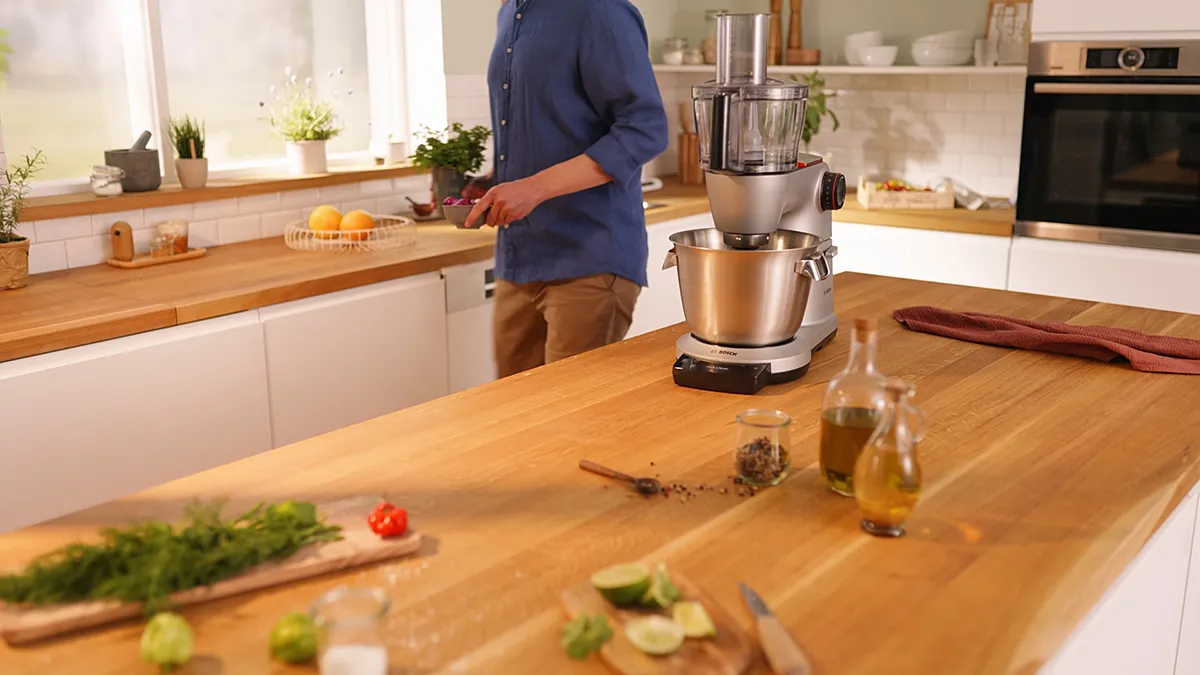 Person using kitchen appliance on wooden counter with fresh ingredients.