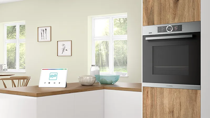 Modern kitchen with wooden countertop, smart home device, and stainless steel oven.