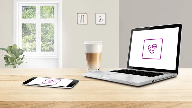 Laptop and smartphone on wooden desk, displaying medical icon, coffee cup, and indoor plants visible.
