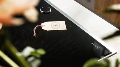 alt-Beige label with red and white string on a black NEFF hob and plants blurred in the foreground.