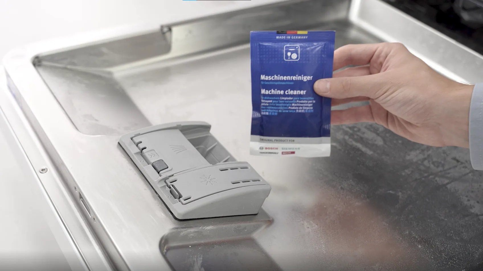 Hand holding a packet of machine cleaner, placed on a Bosch washing machine.