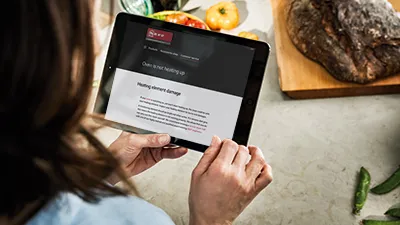 alt-A person in a cosy kitchen, surrounded by a bowl of oranges and a vibrant vase of lemons, navigates to NEFF Self Help content using a smartphone.