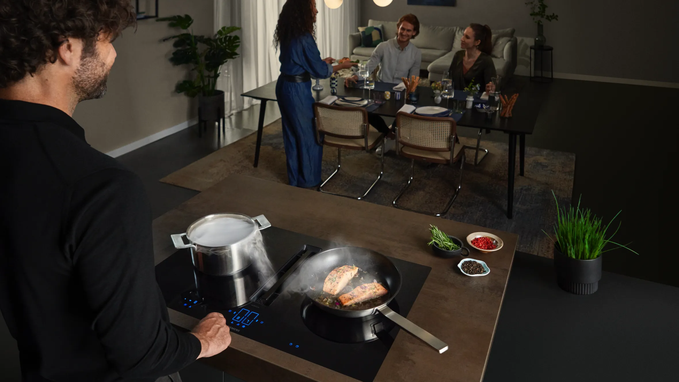 Dinner party with people gathered around a table, while a person is cooking in the foreground.