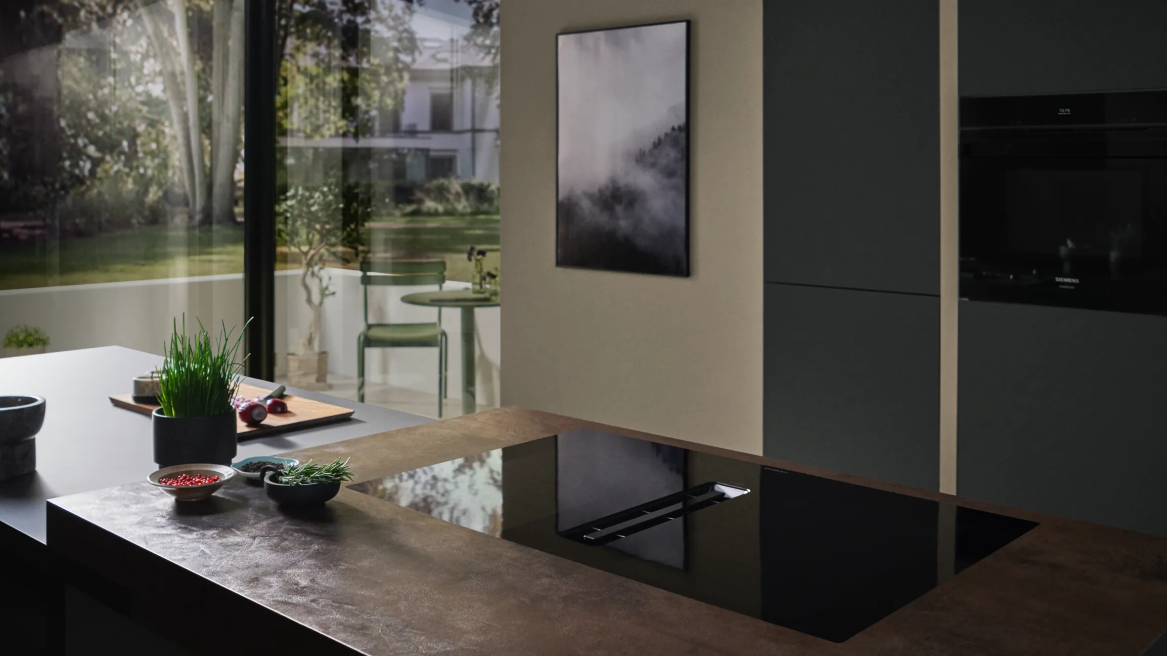 Modernt kök med elegant svart bänkskiva, krukväxter och inramade konstverk på väggen.