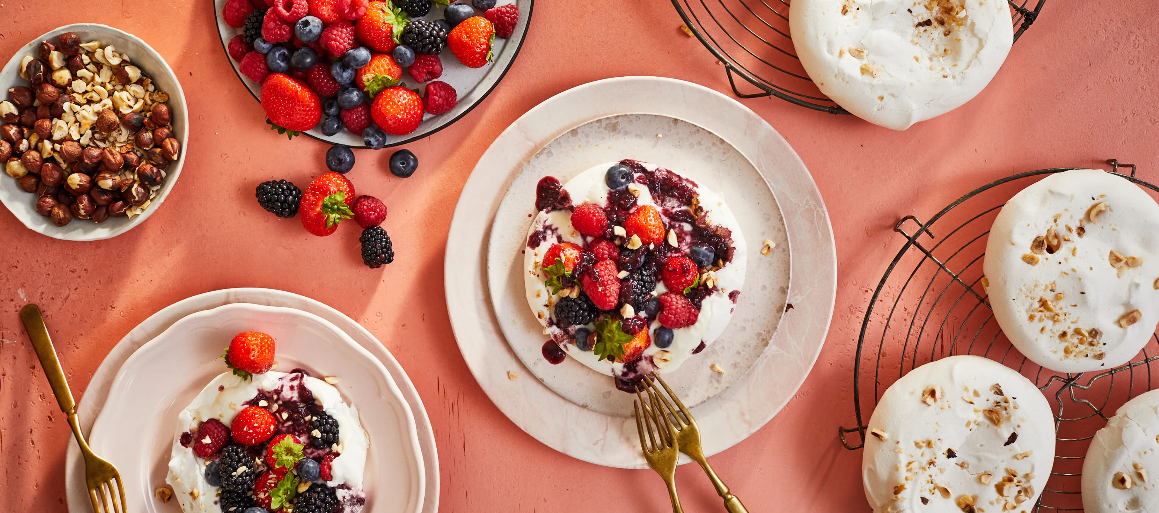 Assortment of fresh berries, granola, and yogurt on plates against a coral background.