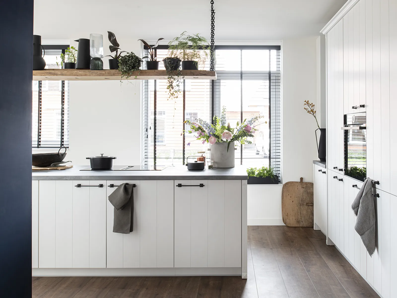 Cuisine moderne avec armoires blanches, étagères en bois, plantes en pot, et grande fenêtre fournissant la lumière naturelle.