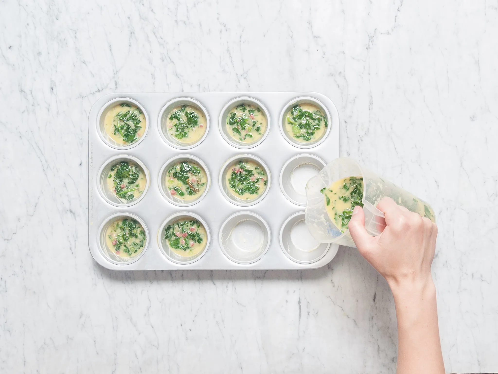 Person stirring spinach in a pan with a wooden spoon on an induction cooktop.