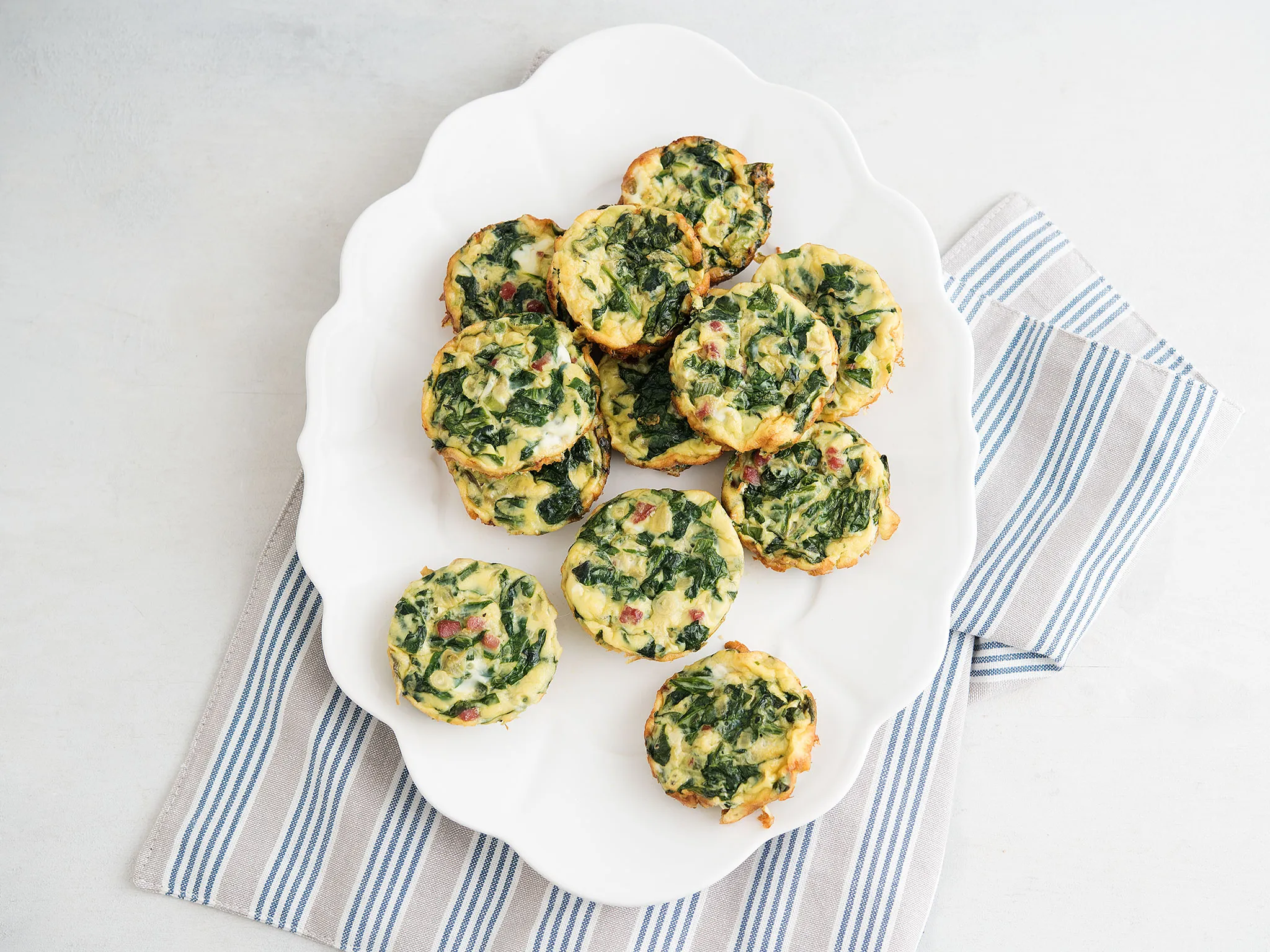 Plate of mini spinach and cheese quiches on a striped cloth on a white surface.