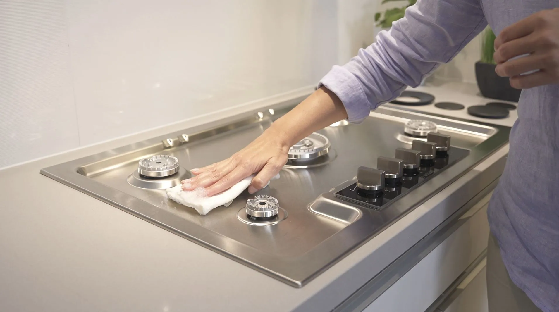 Hands cleaning Bosch stove top burners with cloth, kitchen appliance maintenance.