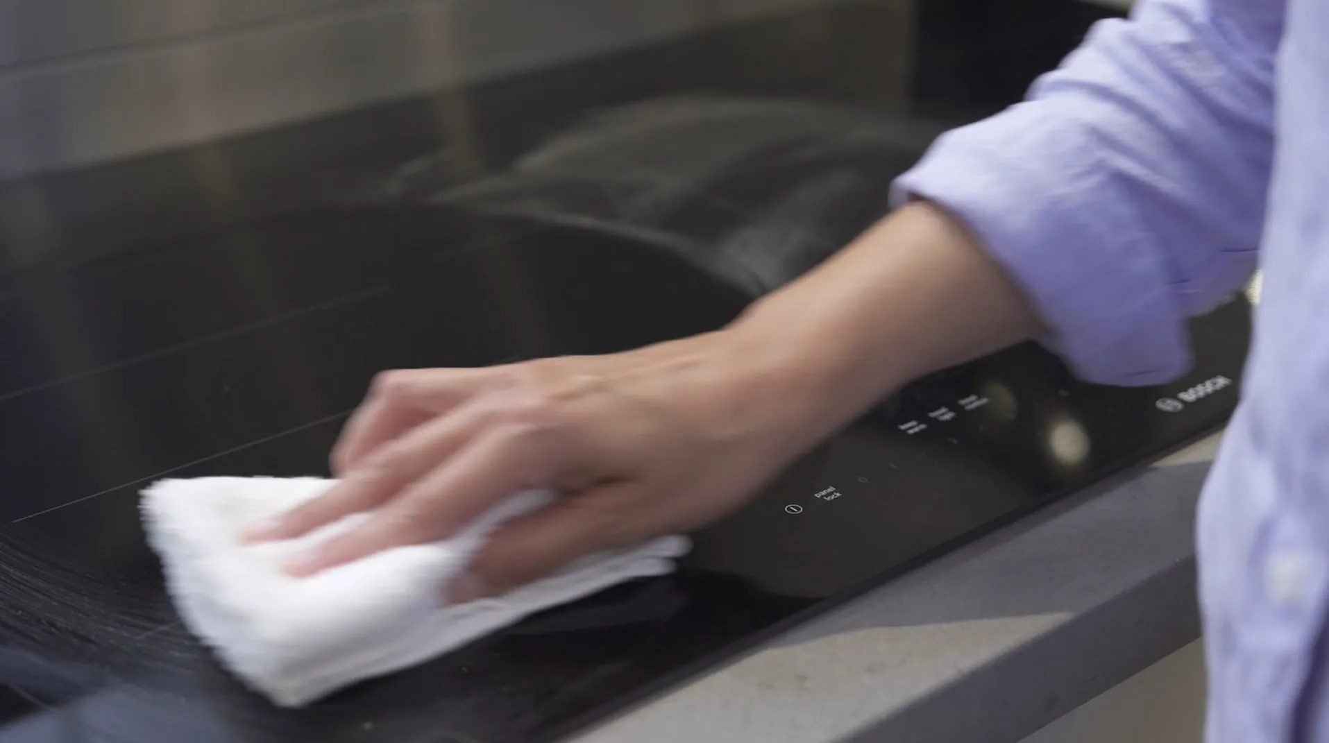 Hands wiping down a Bosch induction cooktop with white towel