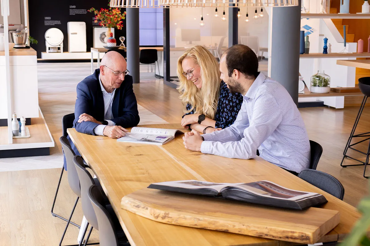 Drie mensen bespreken documenten aan een houten tafel in een moderne kantooromgeving.