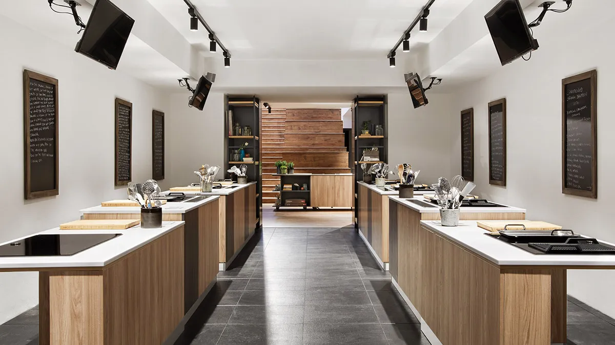 Ampia cucina moderna con tavolo in legno, sedie colorate, scaffali e piante in vaso.
