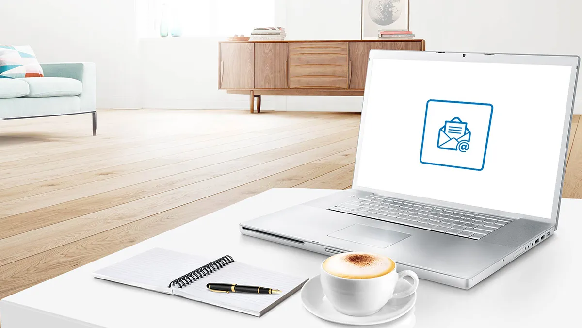 Laptop, taza de café, cuaderno y bolígrafo sobre una mesa blanca en un ambiente moderno.