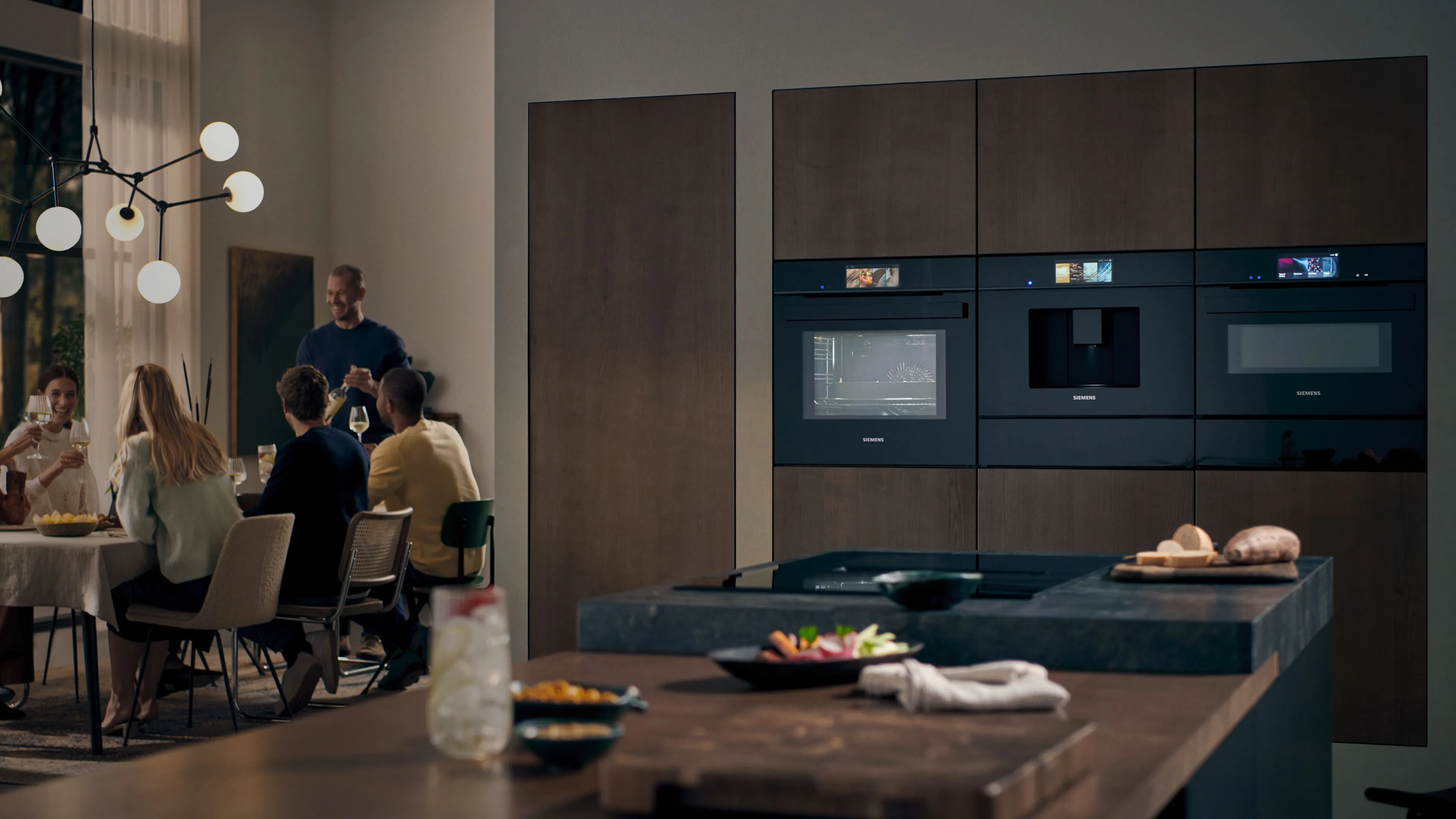 Cozinha moderna com armários escuros, mesa de jantar, e as pessoas se reuniram para uma refeição.