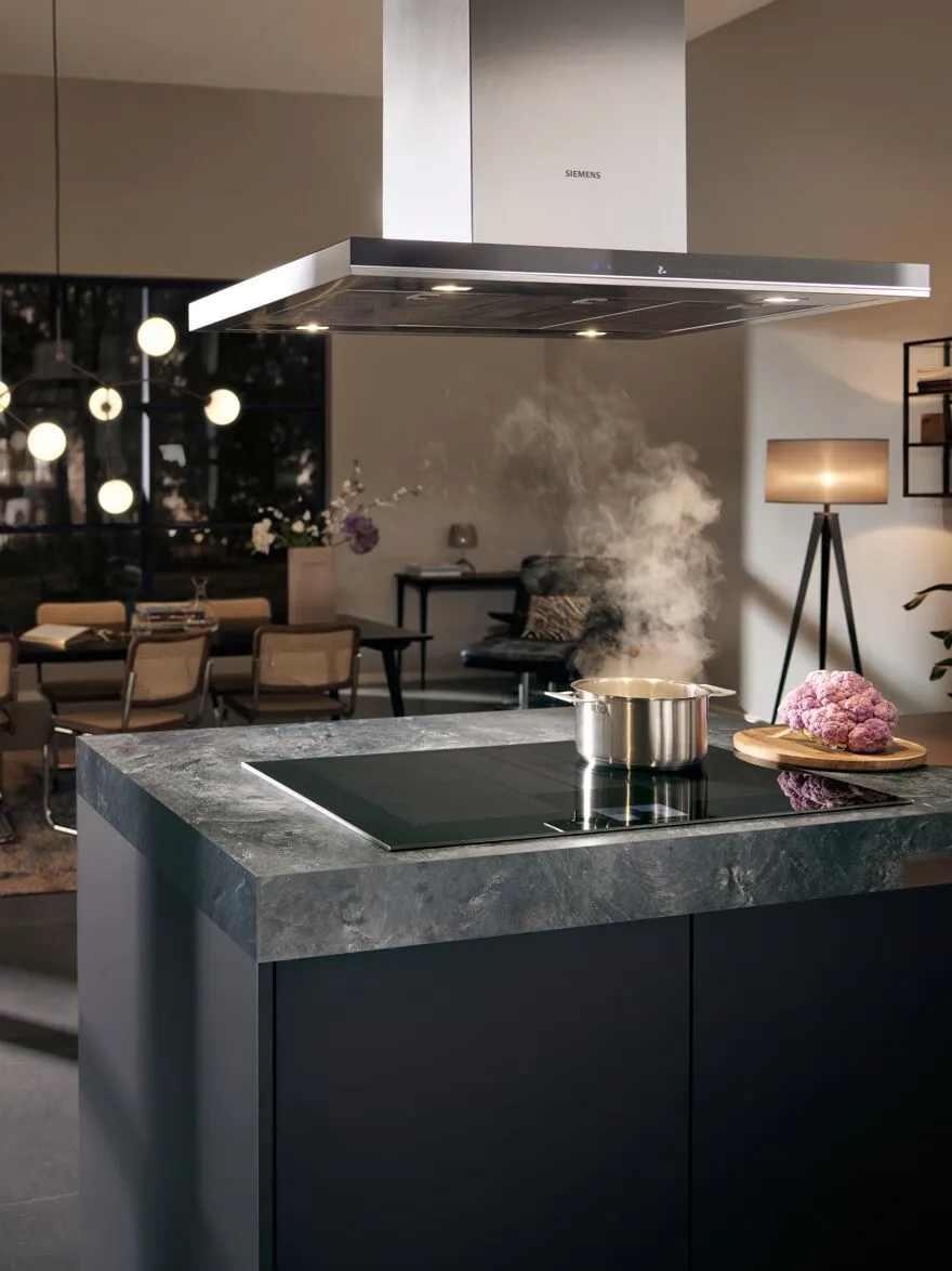 Cozinha moderna com armários pretos elegantes, bancada de mármore e um capuz Siemens que emite vapor.